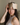 Woman wearing a champagne silk sleep mask on her forehead while sitting on a bed in natural light. 