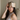 Woman wearing a champagne silk sleep mask on her forehead while sitting on a bed in natural light. 