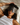 Woman wearing a Dark Gray ZILK Silk sleep mask laying in bed with her head on a white silk pillowcase.