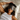Woman wearing a Dark Gray ZILK Silk sleep mask laying in bed with her head on a white silk pillowcase.