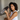 Woman holding a dark gray silk sleep mask in her hands to show the soft, pillowy feel while sitting in a bed.