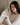 Woman holding a dark gray silk sleep mask in her hands to show the soft, pillowy feel while sitting in a bed.