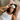 woman wearing a light gray silk sleep mask on her forehead laying in bed on a  pink silk pillowcase