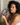 woman with curly hair holding a dark gray silk sleep mask showing the sculpted eye contours that protect eyelashes