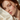 A close-up portrait of a woman with red hair and freckles resting her head on ivory ZILK silk, with warm natural light and a soft blurred background.