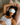 woman wearing a light gray silk sleep mask over her eyes, laying in bed with her head on a light pink silk pillowcase.