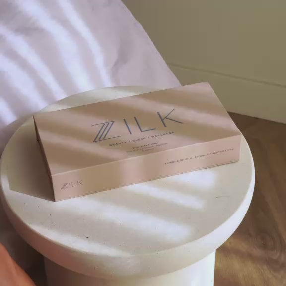 Model opens silk sleep mask box, puts on sculpted eye mask with comfort wrap, and relaxes in bed